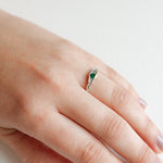 Side view of a hand wearing a silver ring with a green stone set in a natural-shaped band.