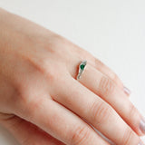 Side view of a hand wearing a silver ring with a green stone set in a natural-shaped band.