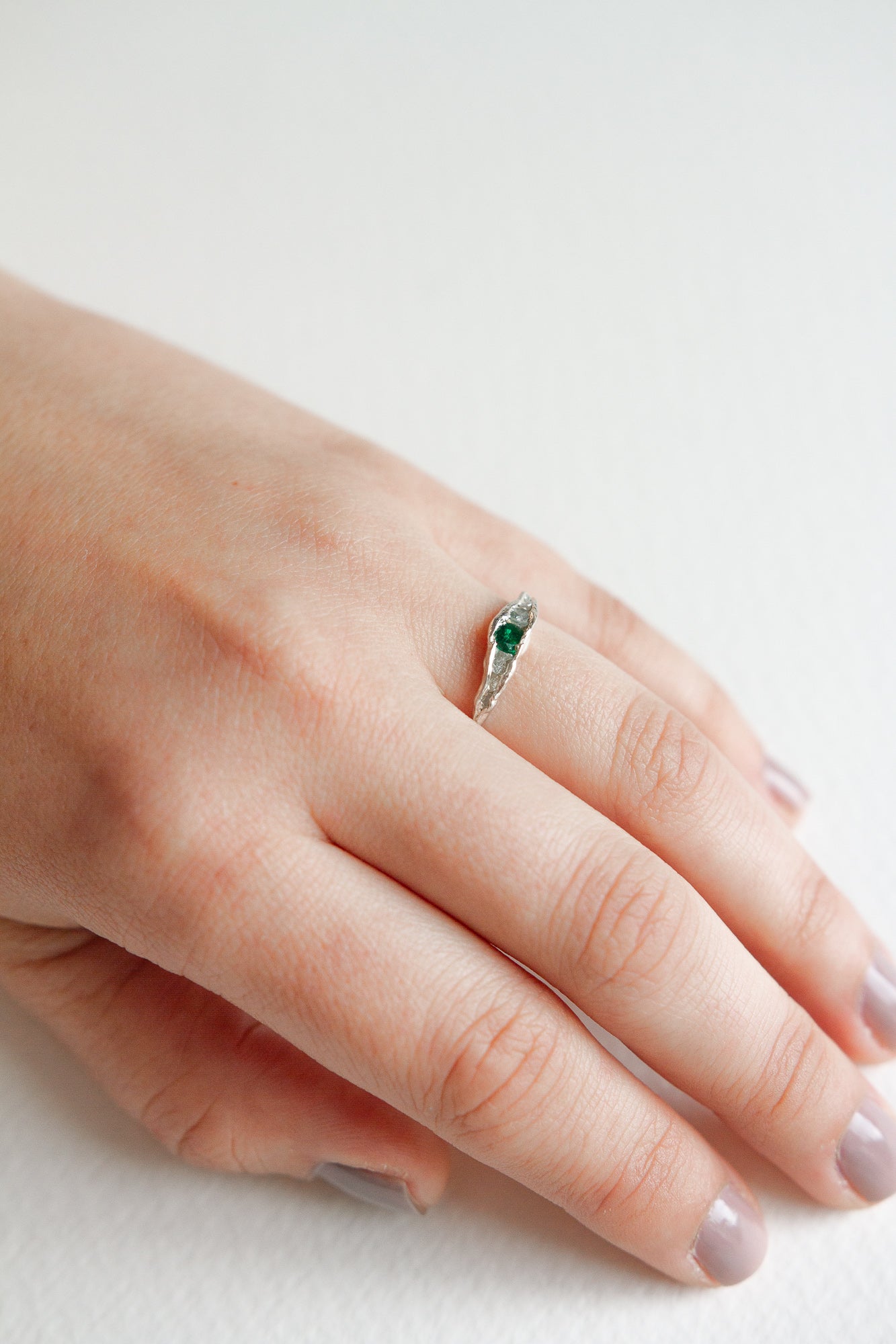 Side view of a hand wearing a silver ring with a green stone set in a natural-shaped band.