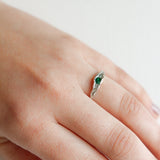 Hand wearing a silver ring with a green gemstone, showing the delicate and minimalist design.