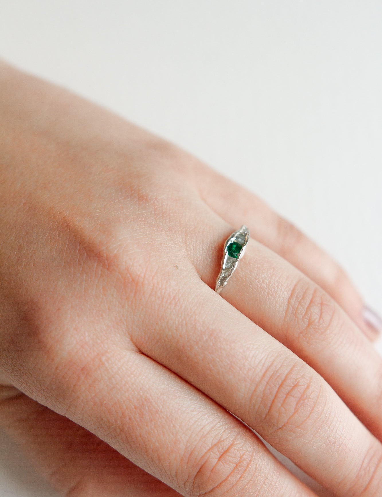 Hand wearing a silver ring with a green gemstone, showing the delicate and minimalist design.