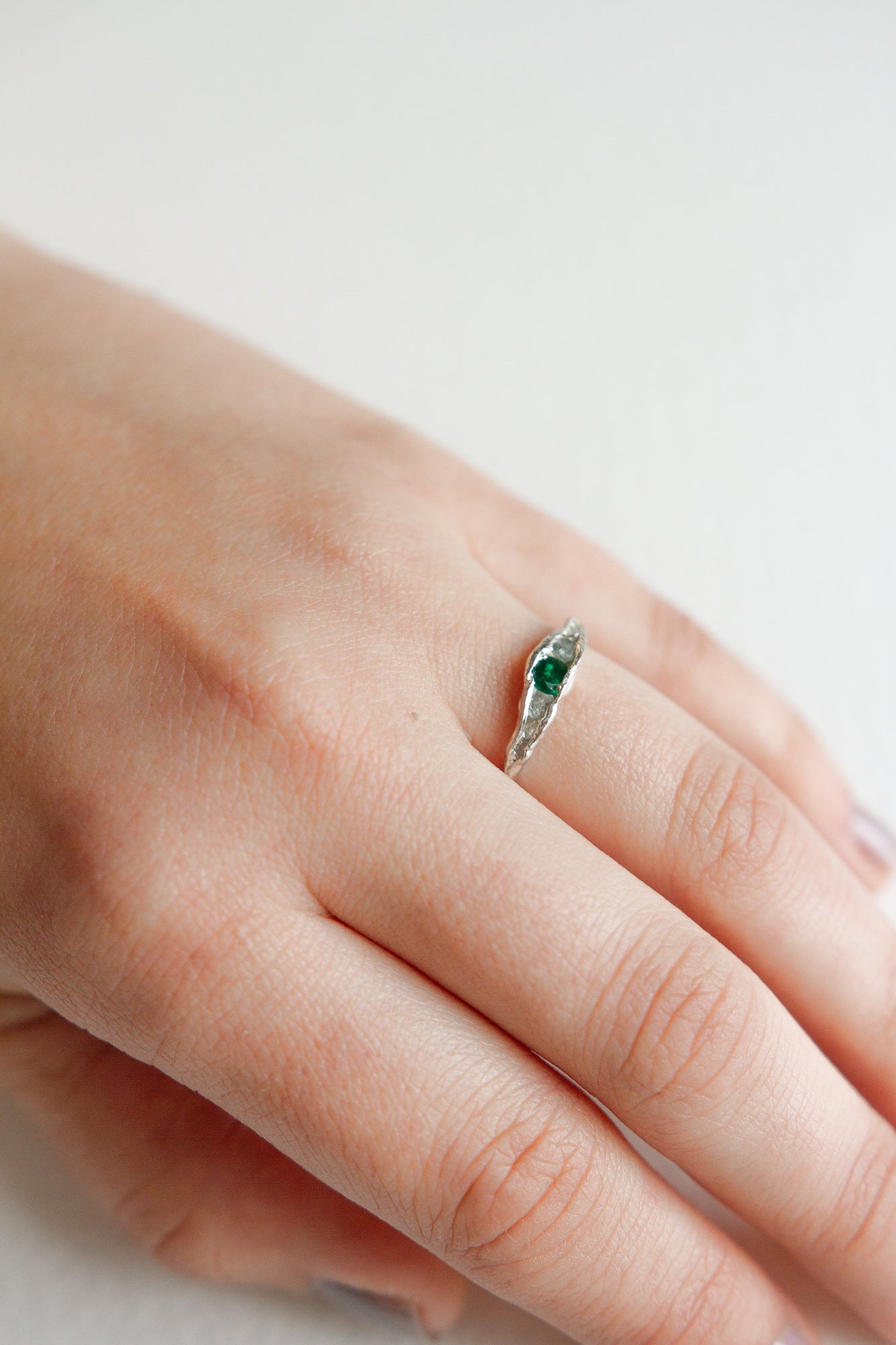 Hand wearing a silver ring with a green gemstone, showing the delicate and minimalist design.