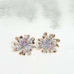 Wild clover stud earrings on a light background with blurred branches, highlighting their botanical design and handcrafted finish.