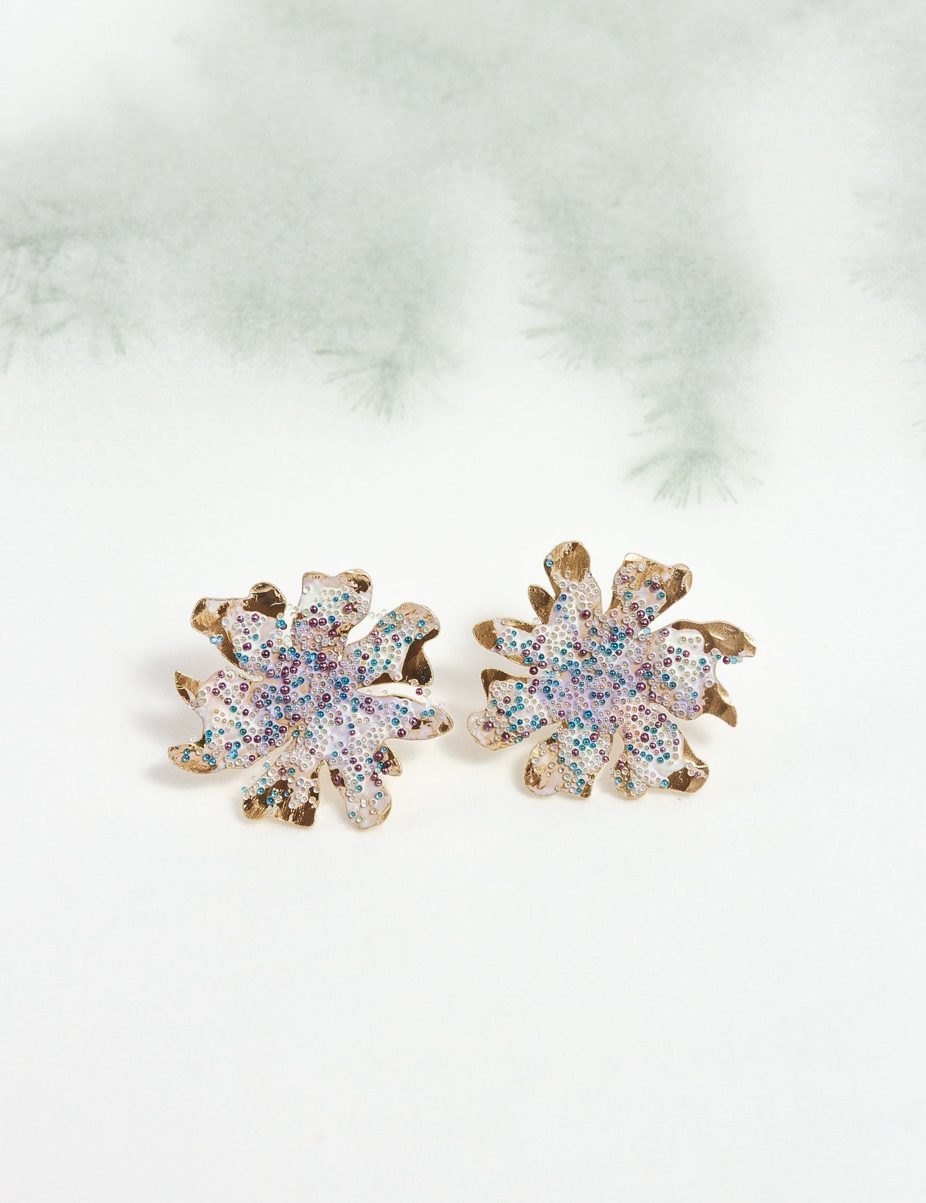 Wild clover stud earrings on a light background with blurred branches, highlighting their botanical design and handcrafted finish.