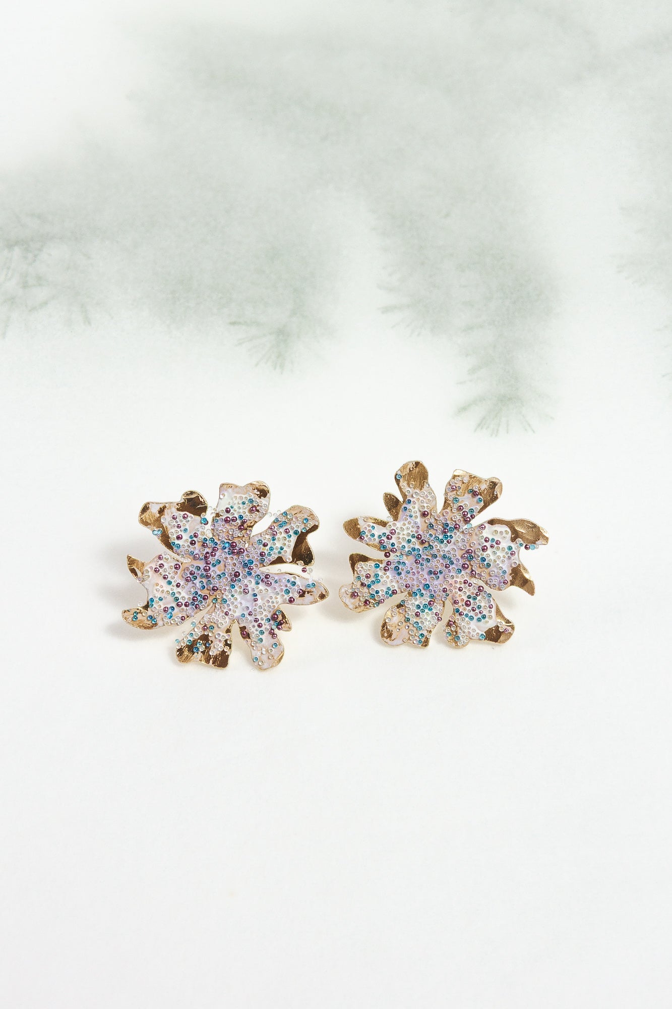 Wild clover stud earrings on a light background with blurred branches, highlighting their botanical design and handcrafted finish.