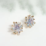 Wild clover stud earrings on a light background with blurred branches, highlighting their botanical design and handcrafted finish.