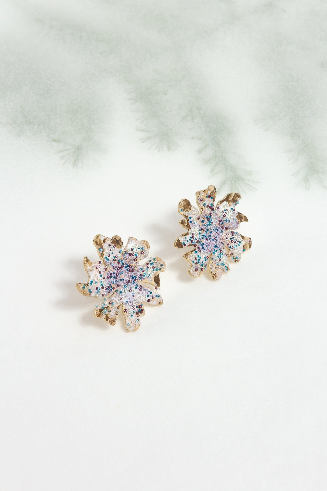 Wild clover stud earrings on a light background with blurred branches, highlighting their botanical design and handcrafted finish.