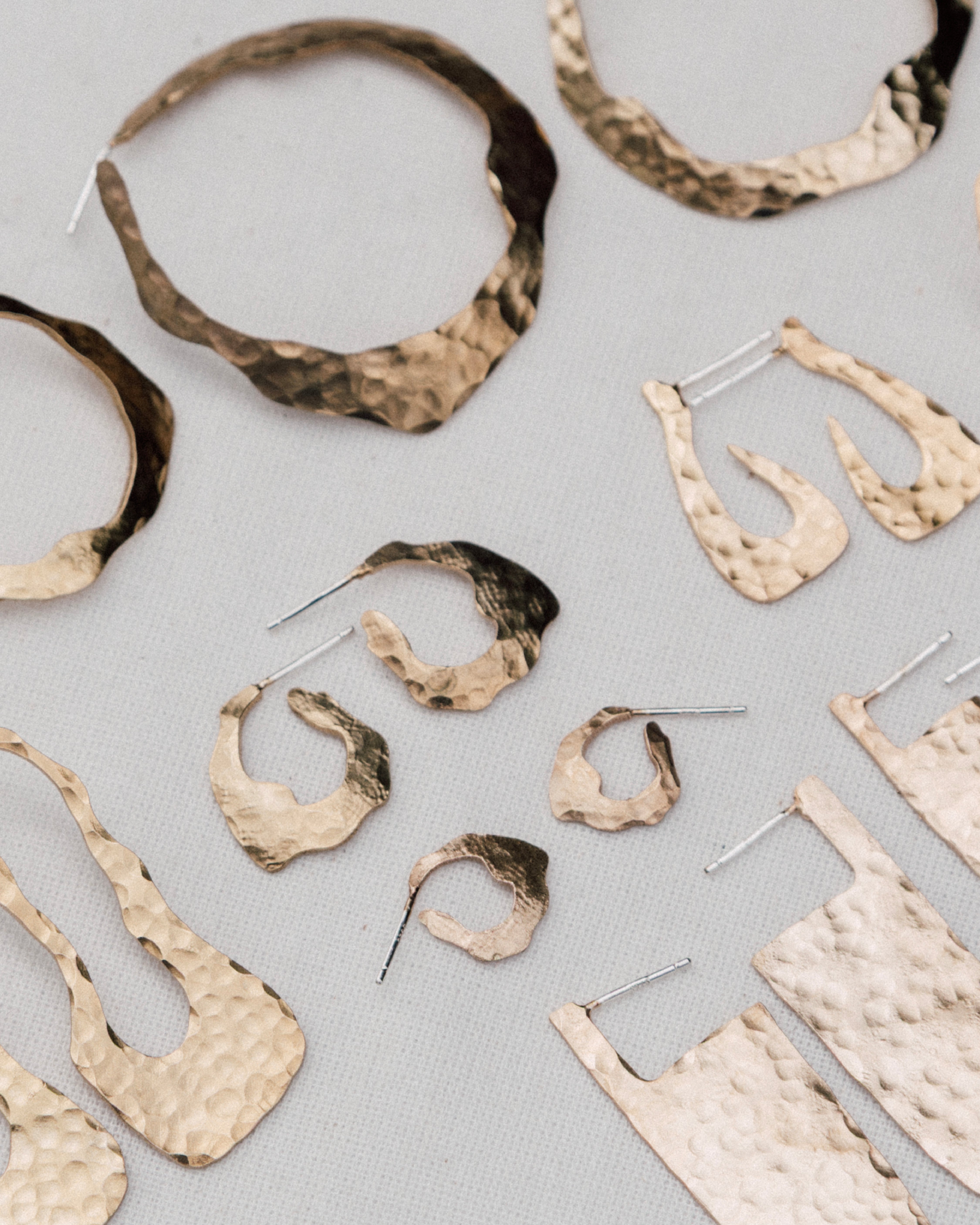 Assortment of handcrafted hammered gold earrings in organic shapes, displayed on a neutral fabric background.