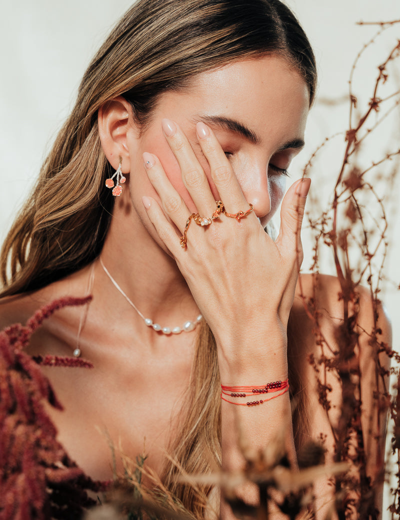 Model wearing the agraz Earrings in a natural setting with branches and warm tones.