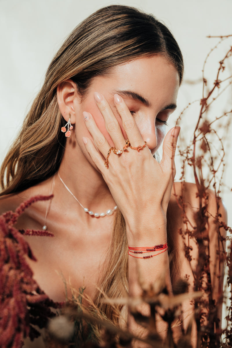 Model wearing the agraz Earrings in a natural setting with branches and warm tones.