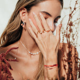 Model wearing the agraz Earrings in a natural setting with branches and warm tones.