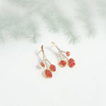 agraz earrings on a light background with blurred branches, showcasing their organic shape and handcrafted finish.