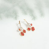 agraz earrings on a light background with blurred branches, showcasing their organic shape and handcrafted finish.