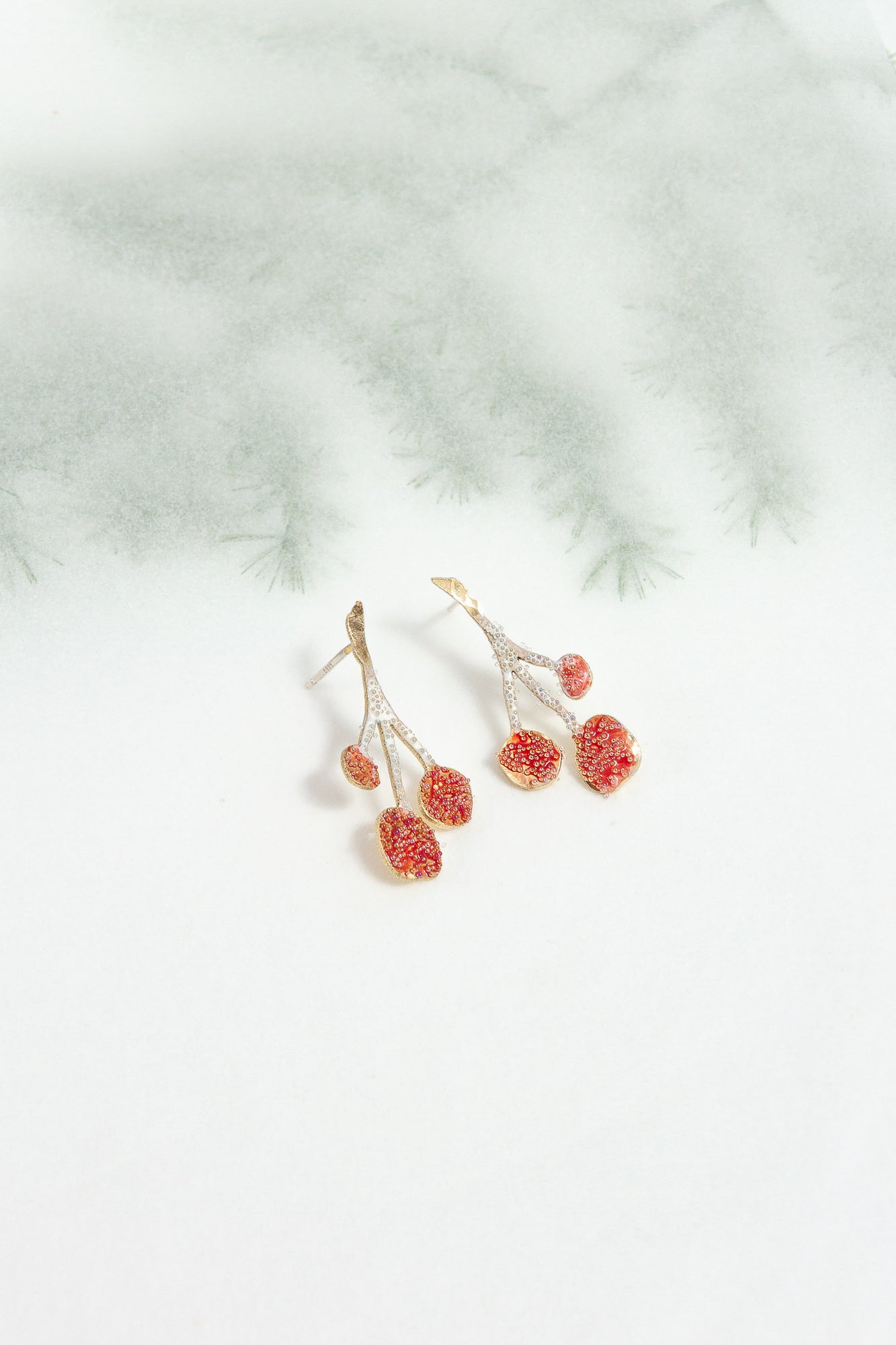 agraz earrings on a light background with blurred branches, showcasing their organic shape and handcrafted finish.