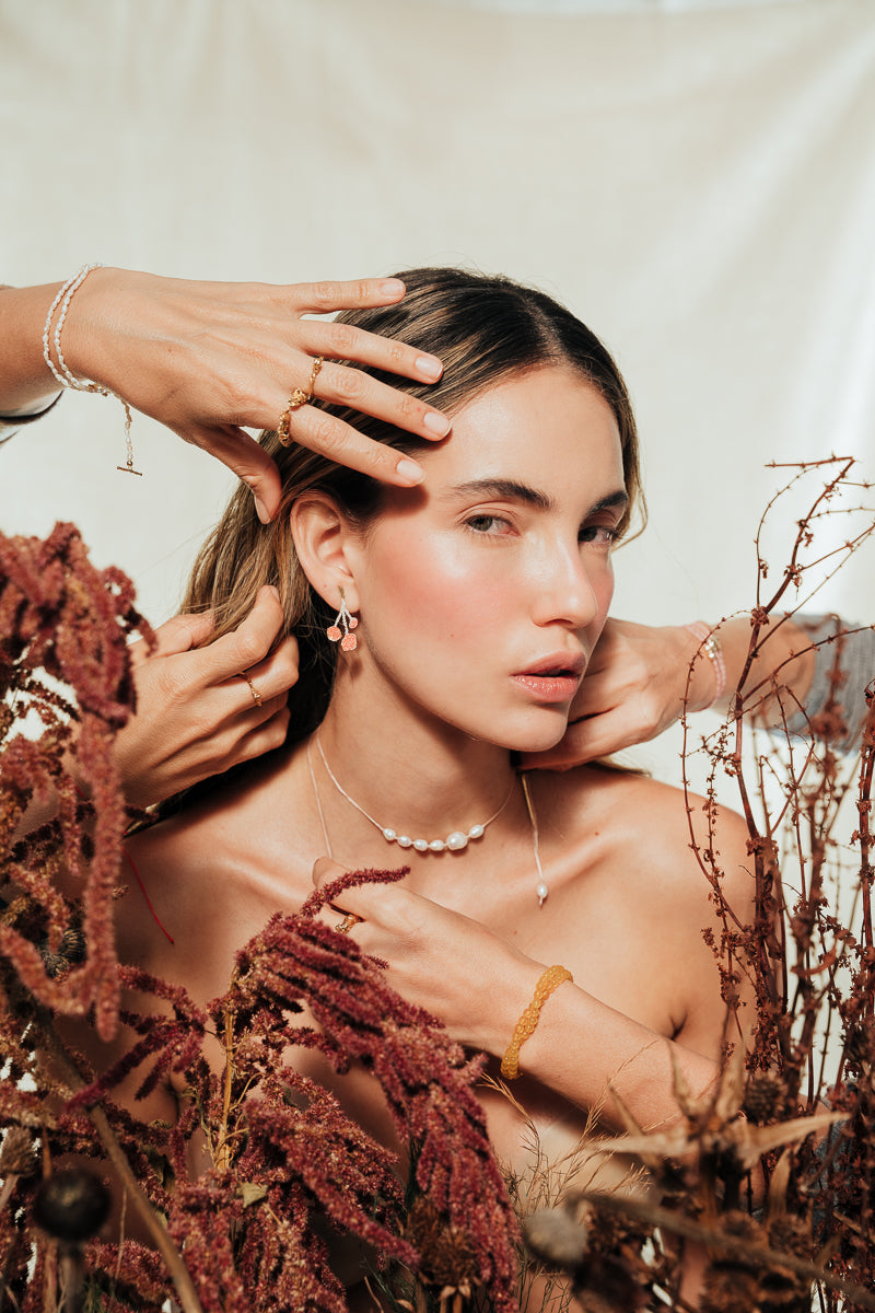 Stylized scene with the model and hands adjusting the agraz Earrings in a botanical setting.