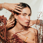 Stylized scene with the model and hands adjusting the agraz Earrings in a botanical setting.