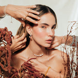 Stylized scene with the model and hands adjusting the agraz Earrings in a botanical setting.