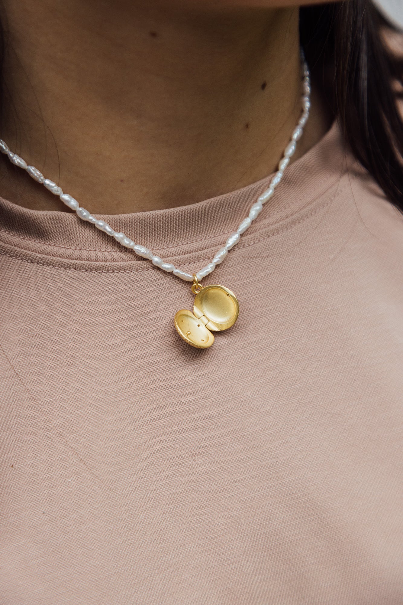 CÂPÂ pearl locket, crafted from gold-plated bronze, cultured pearls, and aquamarine-colored cubic zirconia; worn around the neck by the model.