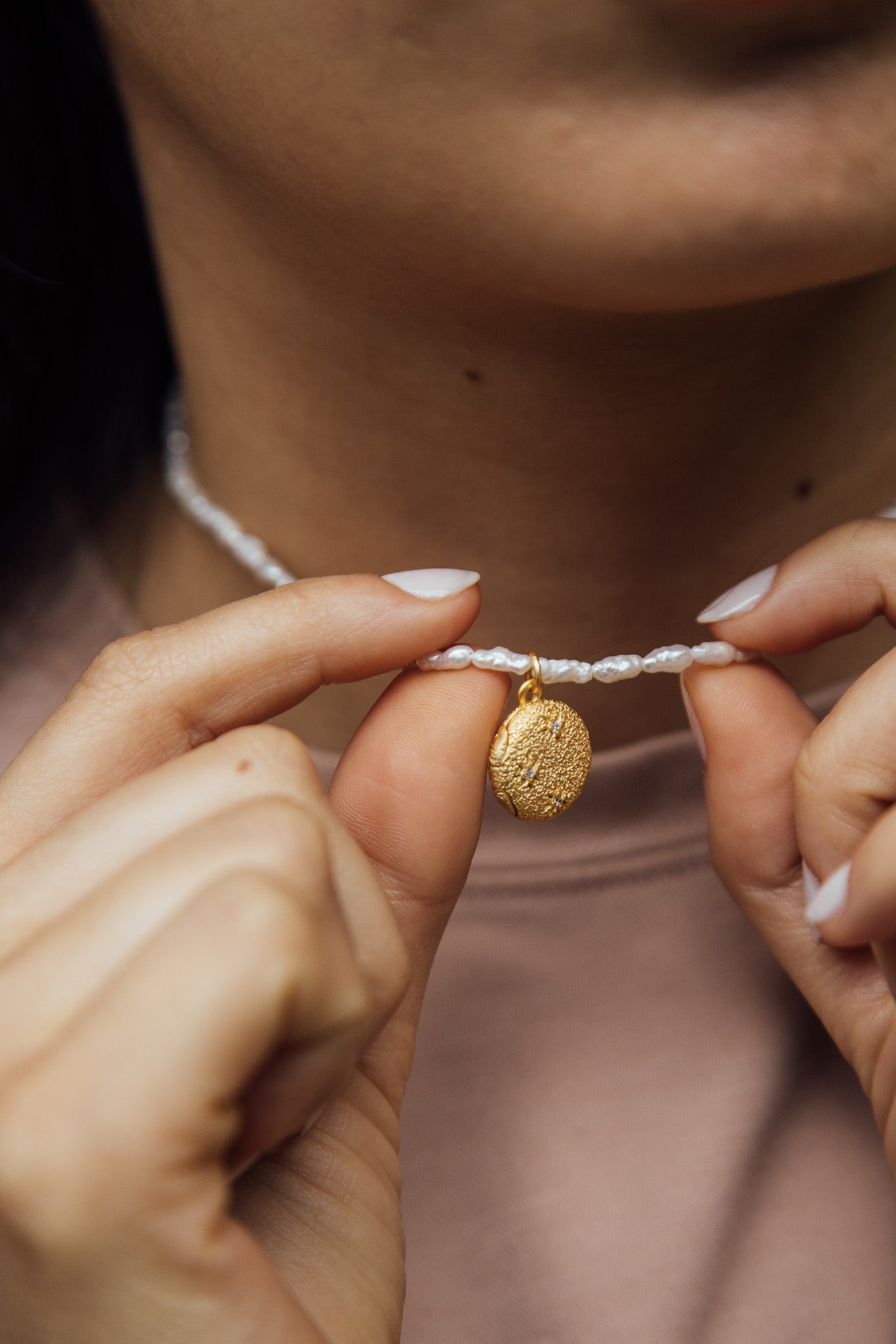 CÂPÂ pearl locket, crafted from gold-plated bronze, cultured pearls, and aquamarine-colored cubic zirconia; worn around the neck by the model.