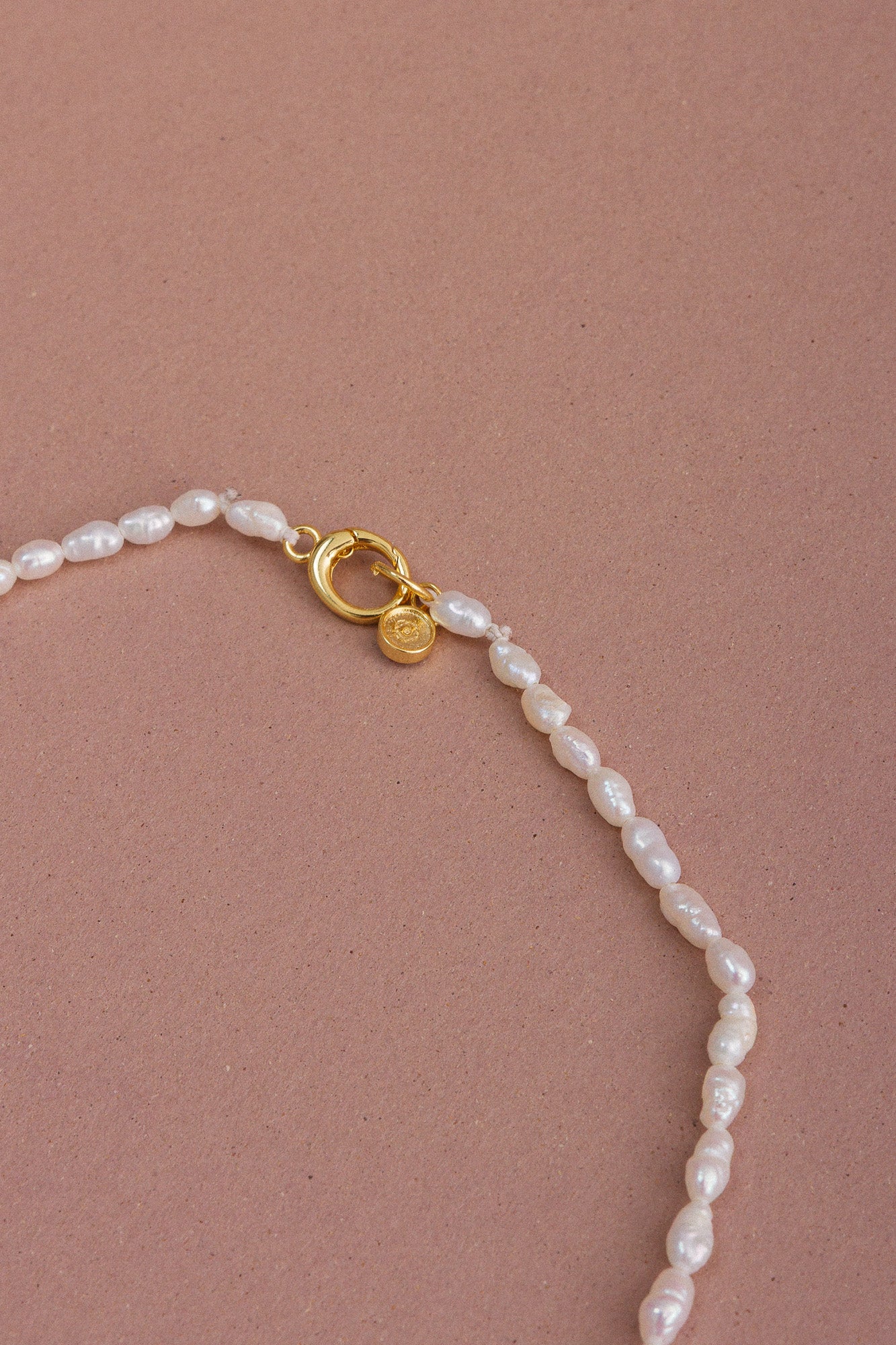 Detail featuring a clasp and pearl beads; openwork "CÂPÂ" pearl locket made of gold-plated bronze, featuring cultured pearls and aquamarine-colored cubic zirconia set against a pale pink background.