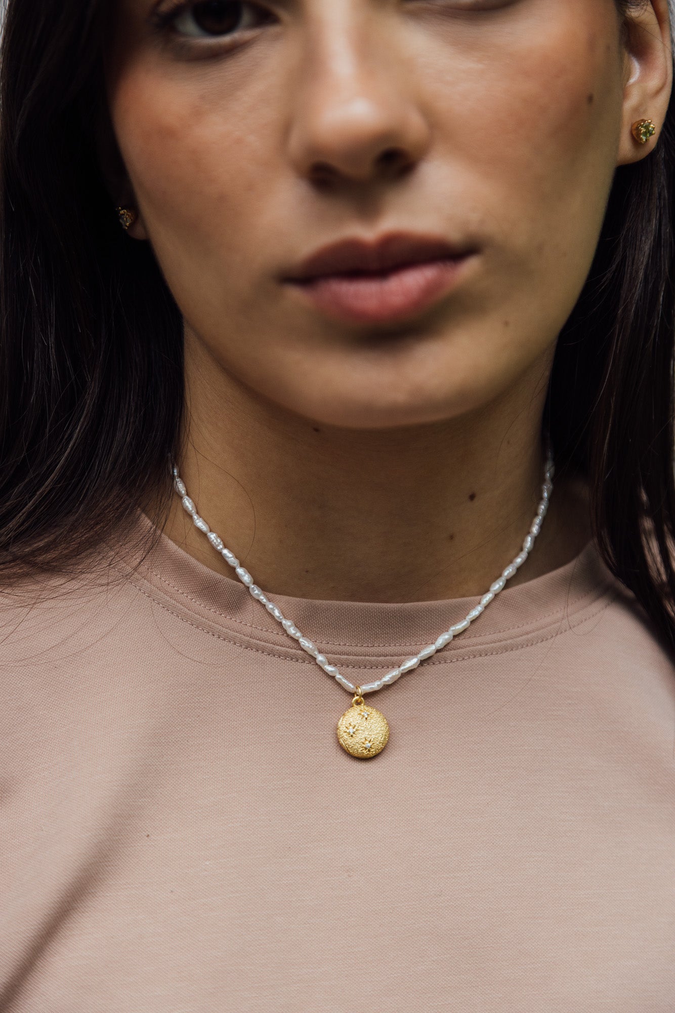 CÂPÂ pearl locket, crafted from gold-plated bronze, cultured pearls, and aquamarine-colored cubic zirconia; worn around the neck by the model.
