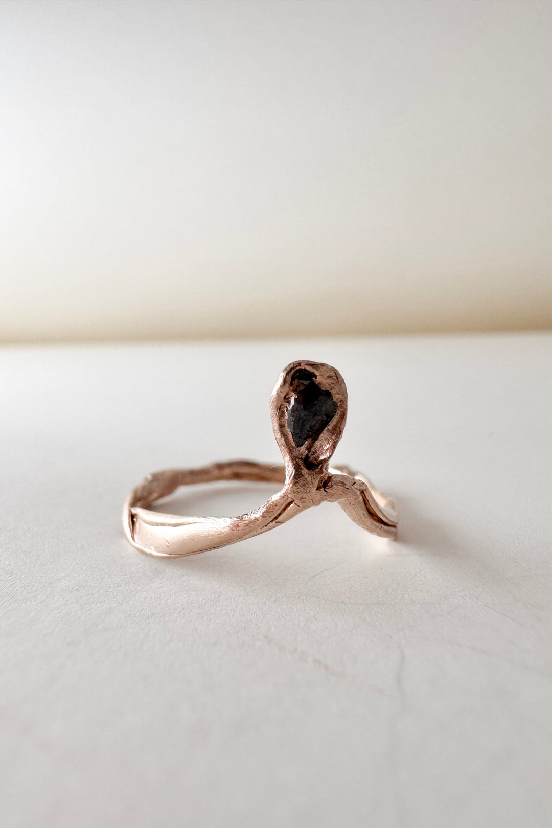 14k rose gold ring with a salt-and-pepper diamond in an organic sculpted band, shown front-facing on a white surface.