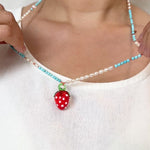 Close‑up of a child’s neckline in a white top, featuring the Strawberry Necklace with its red glass strawberry pendant resting at the center.