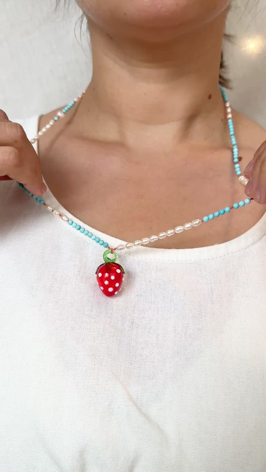 Close‑up of a child’s neckline in a white top, featuring the Strawberry Necklace with its red glass strawberry pendant resting at the center.