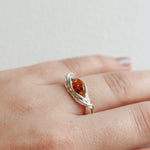 Close-up of a silver ring with a vibrant orange gemstone worn on the hand, highlighting its artisanal form.