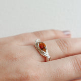 Close-up of a silver ring with a vibrant orange gemstone worn on the hand, highlighting its artisanal form.