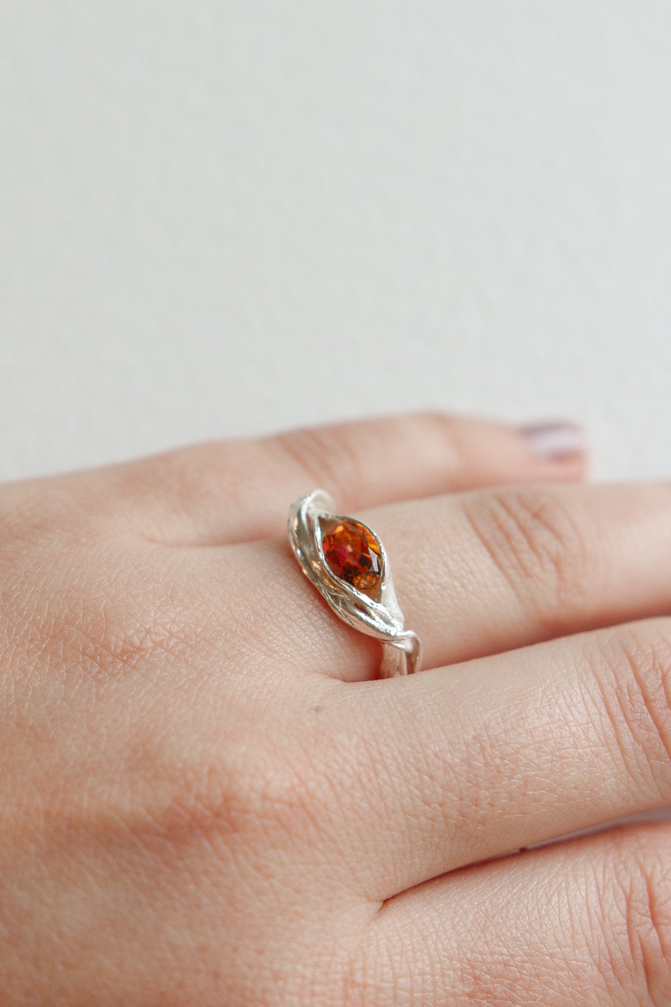 Close-up of a silver ring with a vibrant orange gemstone worn on the hand, highlighting its artisanal form.