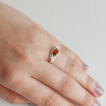 Hand wearing a silver ring with an orange gemstone, showcasing the elegant and natural shape of the band.