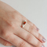Hand wearing a silver ring with an orange gemstone, showcasing the elegant and natural shape of the band.