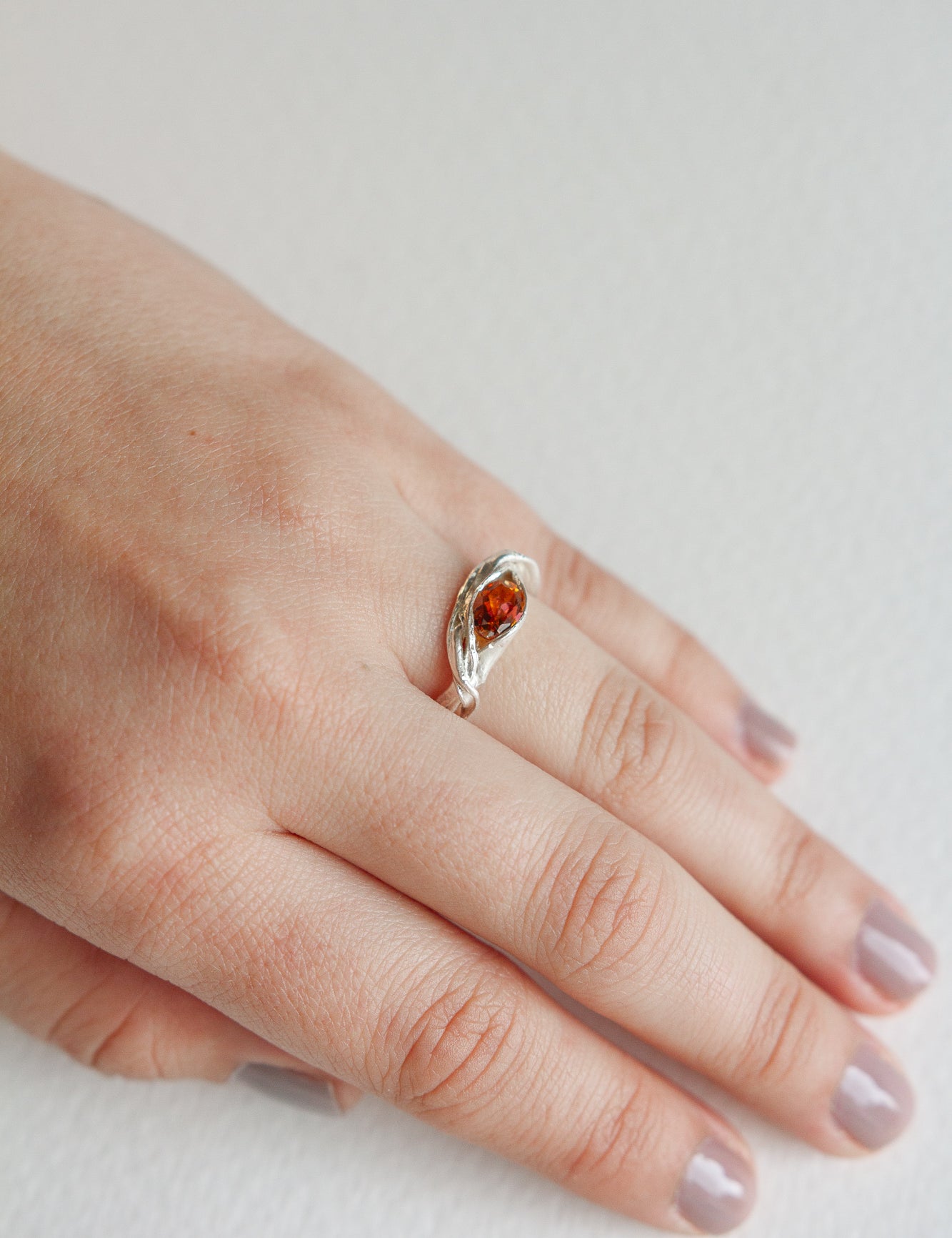 Hand wearing a silver ring with an orange gemstone, showcasing the elegant and natural shape of the band.