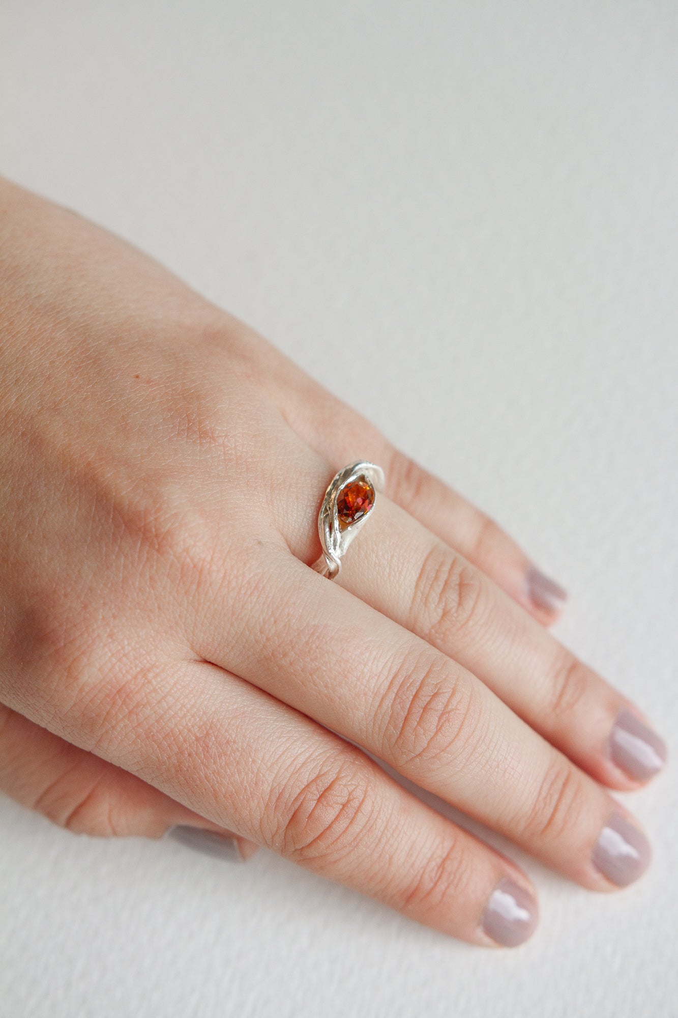 Hand wearing a silver ring with an orange gemstone, showcasing the elegant and natural shape of the band.