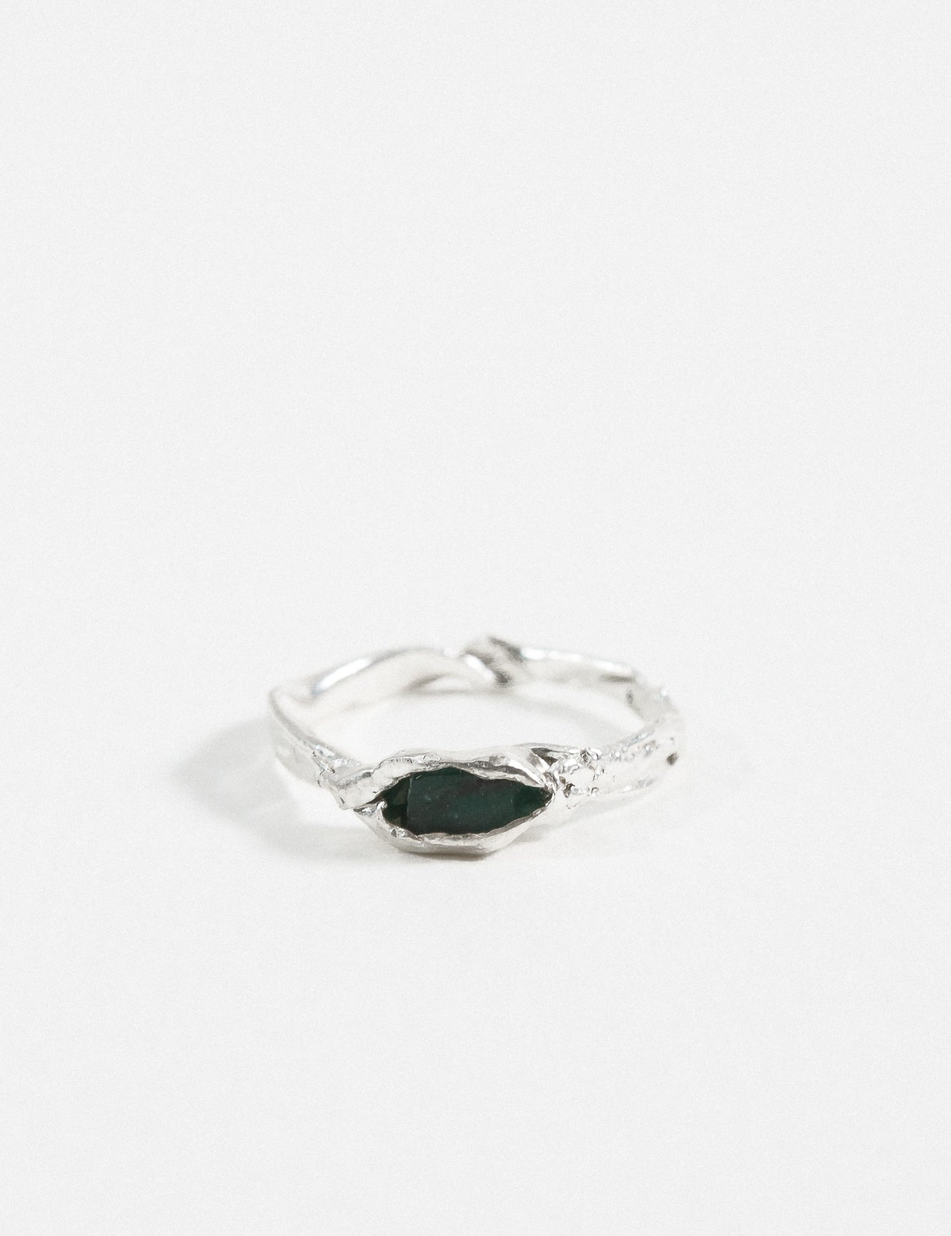 Front view of the sterling silver Refuge Ring showcasing a raw emerald embedded in an organic band, on a white background.