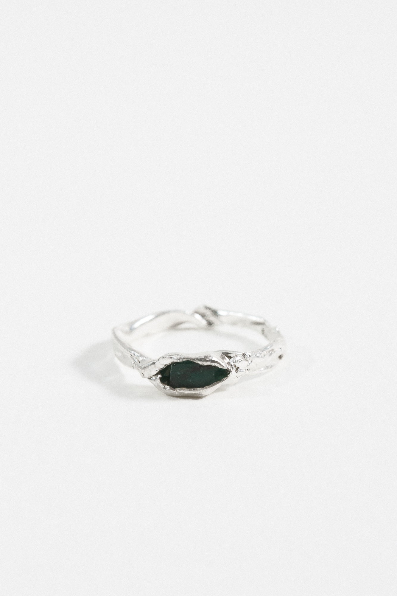 Front view of the sterling silver Refuge Ring showcasing a raw emerald embedded in an organic band, on a white background.