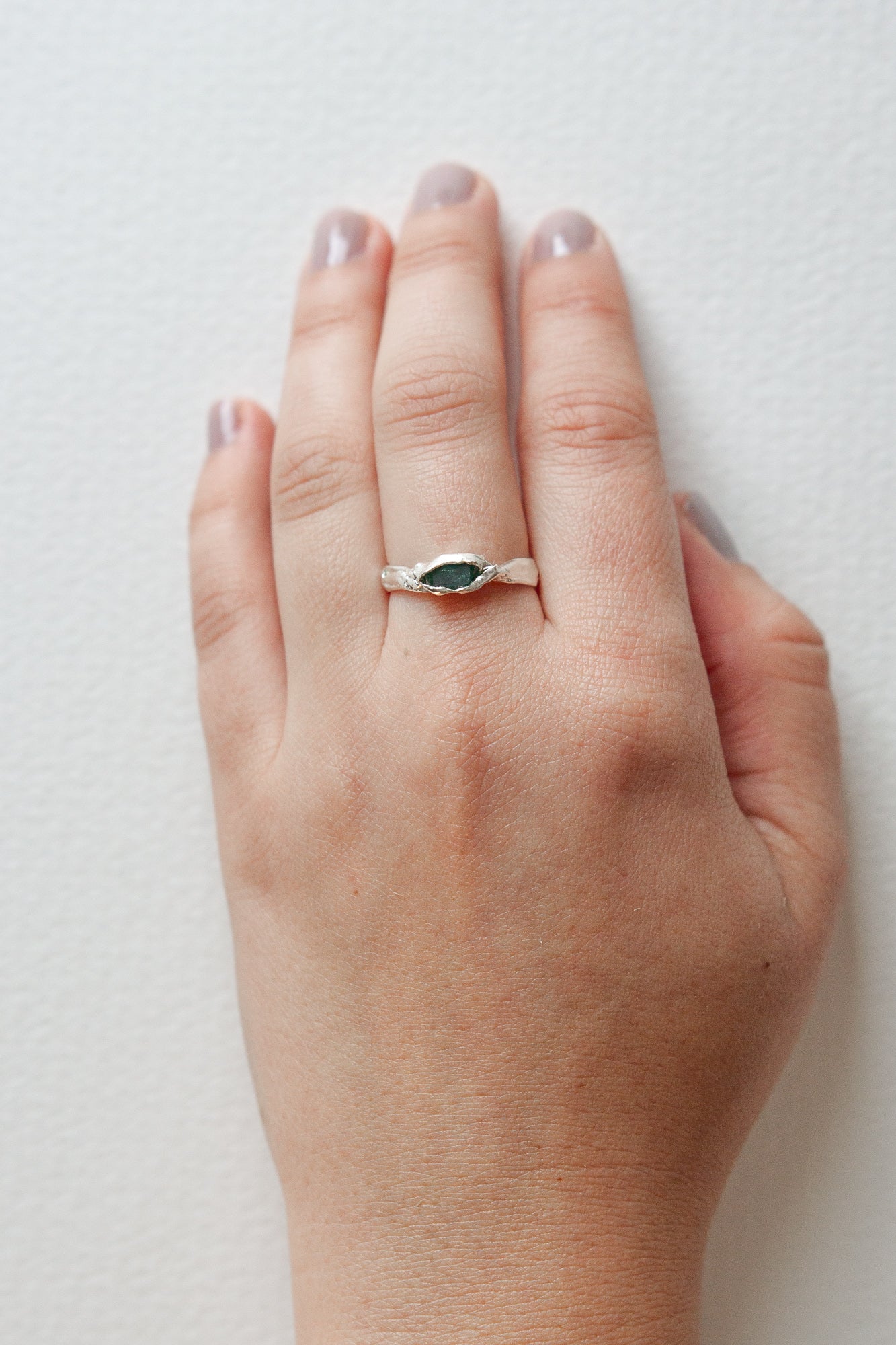 Refuge Ring with raw emerald in sterling silver worn on a hand, seen from a different angle, against a white backdrop.