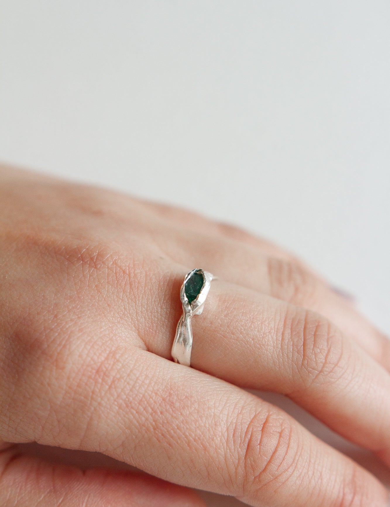 Sterling silver Refuge Ring with a raw emerald worn on a hand, photographed against a light neutral background.