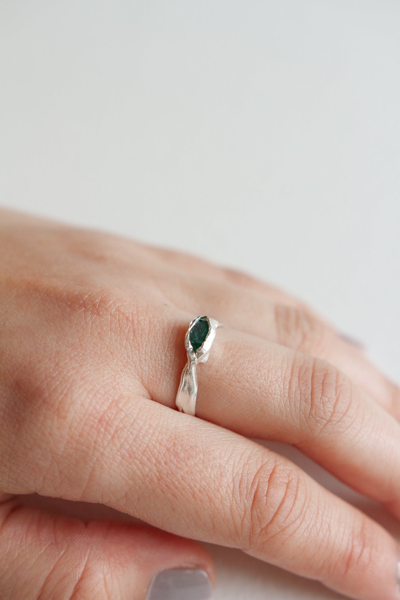 Sterling silver Refuge Ring with a raw emerald worn on a hand, photographed against a light neutral background.