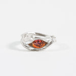 Silver ring with an organic band design and a central orange gemstone, photographed on a white background.