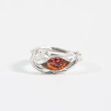 Silver ring with an organic band design and a central orange gemstone, photographed on a white background.