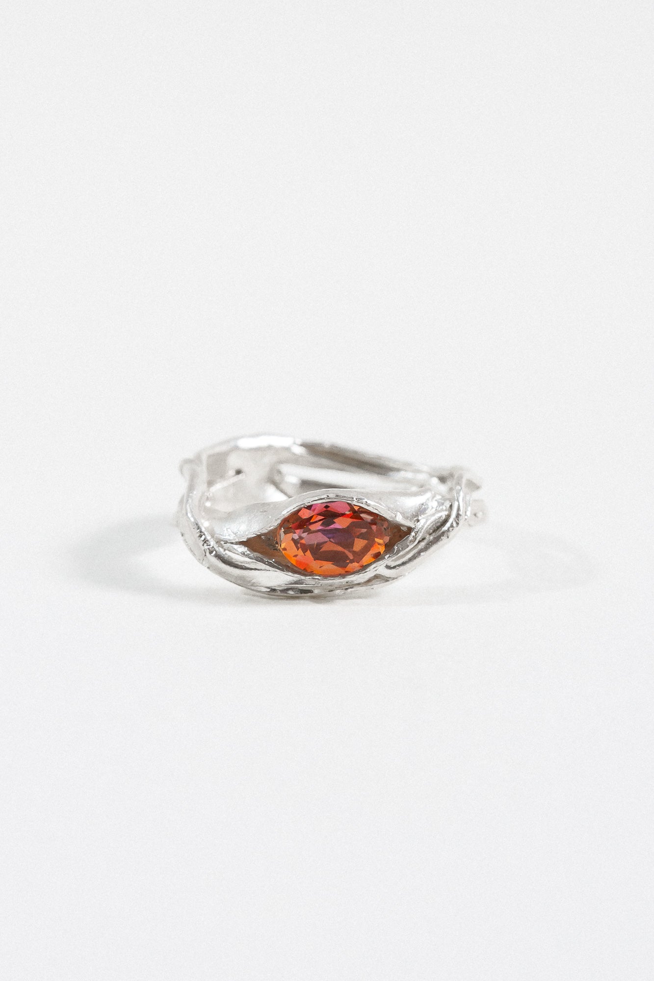 Silver ring with an organic band design and a central orange gemstone, photographed on a white background.