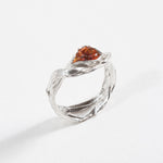 Angled view of a silver ring featuring a textured band and a teardrop-shaped orange stone.