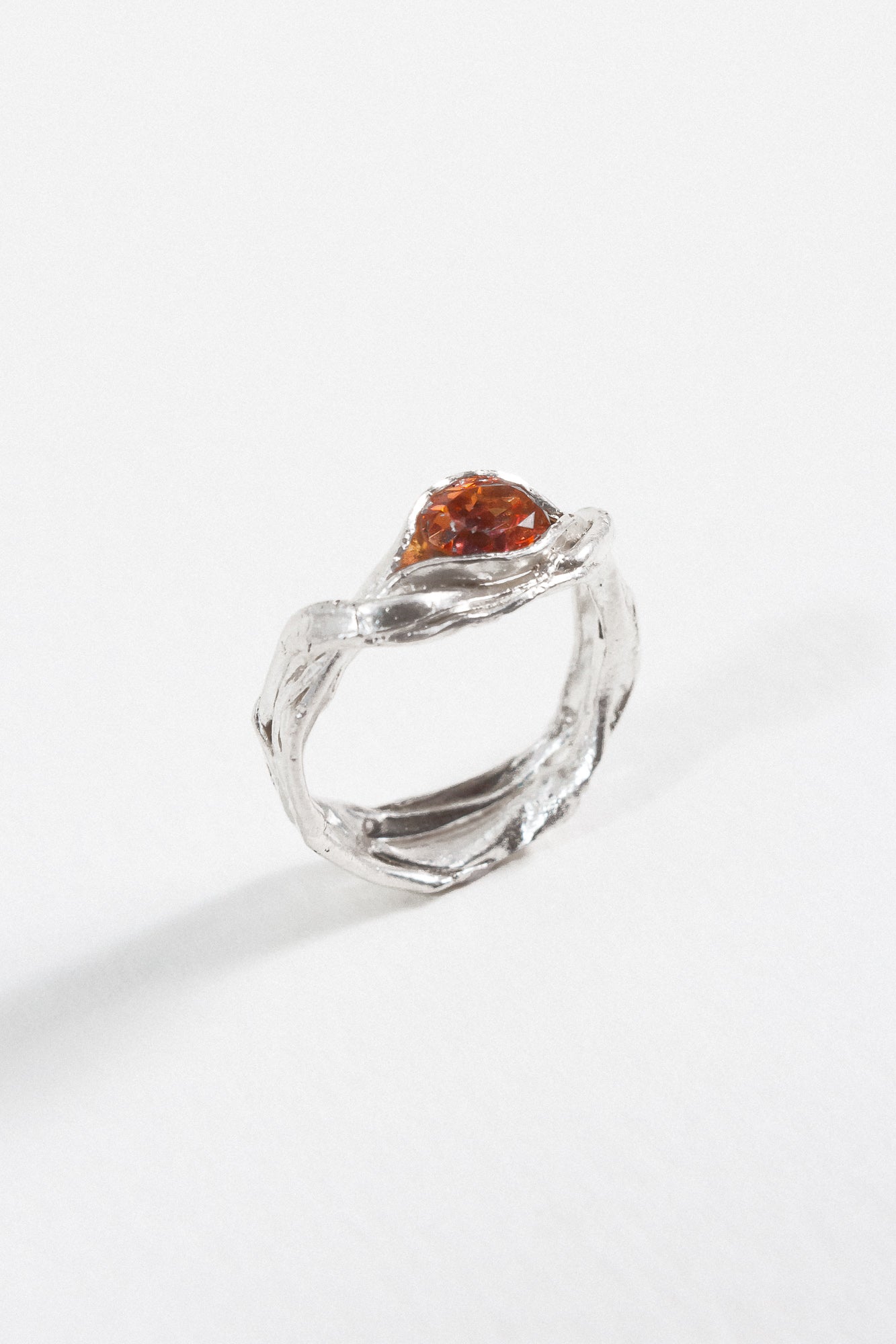 Angled view of a silver ring featuring a textured band and a teardrop-shaped orange stone.