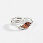 Side view of a silver ring with a sculptural band and a warm orange gemstone centerpiece. 