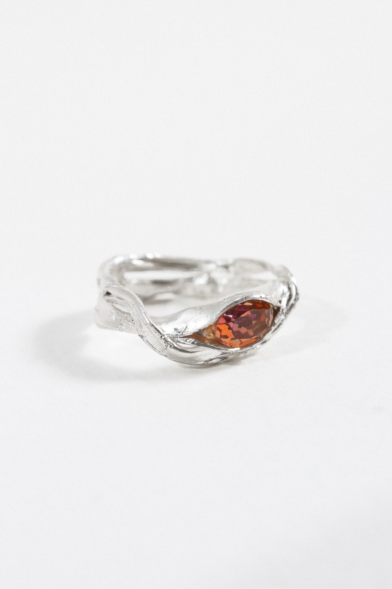 Side view of a silver ring with a sculptural band and a warm orange gemstone centerpiece. 