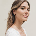 Portrait of a young woman with long hair wearing a single gold star stud earring, against a soft neutral background.