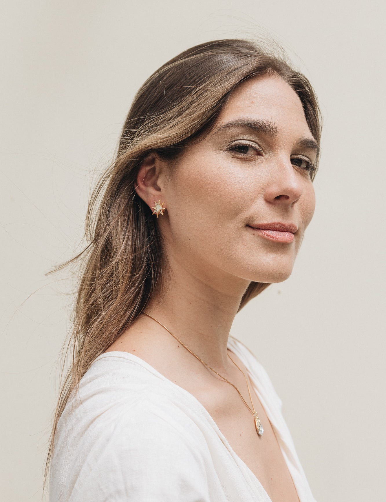 Portrait of a young woman with long hair wearing a single gold star stud earring, against a soft neutral background.