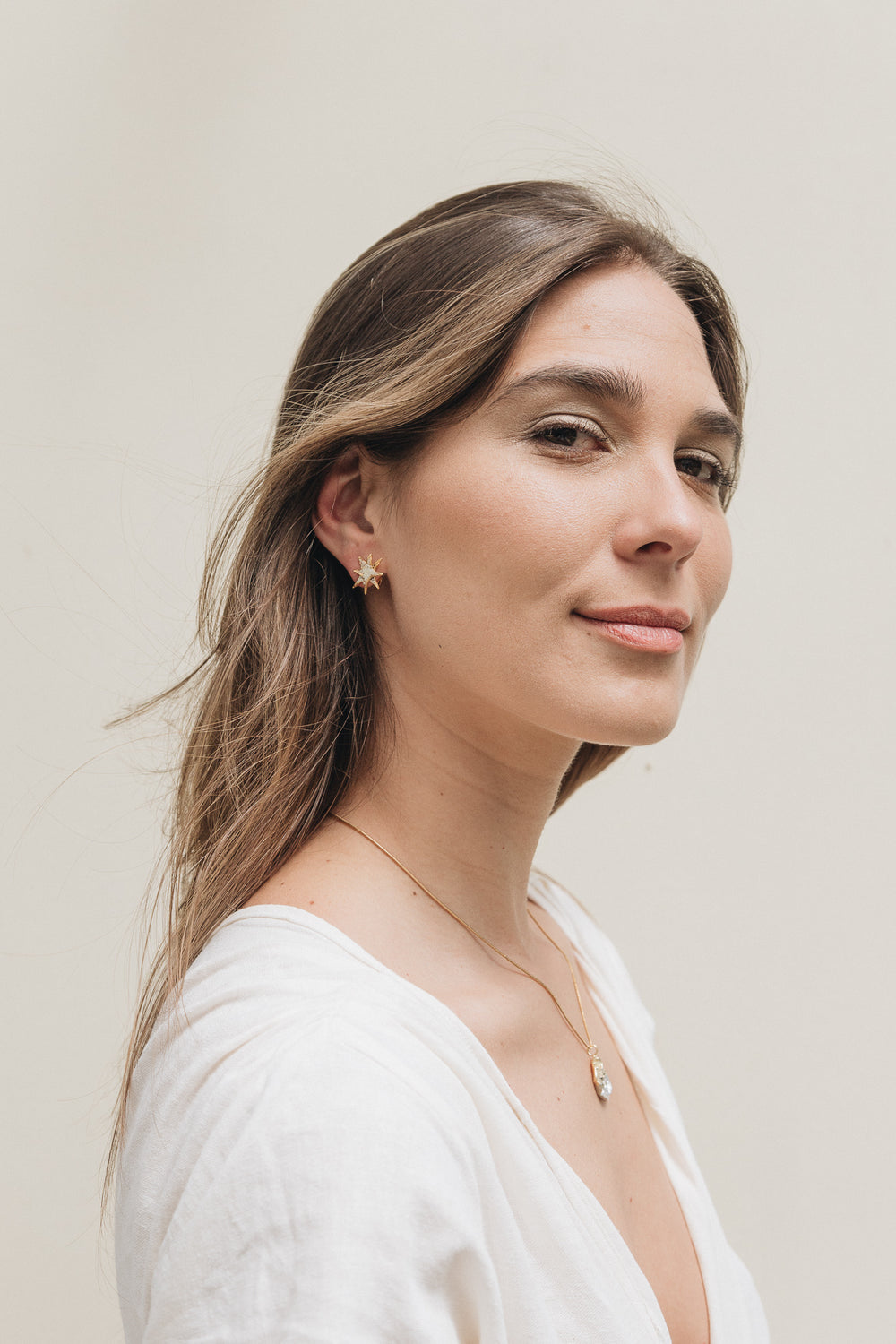 Portrait of a young woman with long hair wearing a single gold star stud earring, against a soft neutral background.